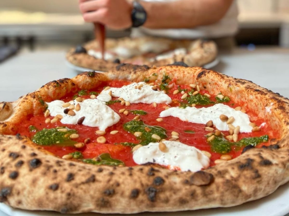 Pizza de tomàquet, burrata i pesto a sobre una taula